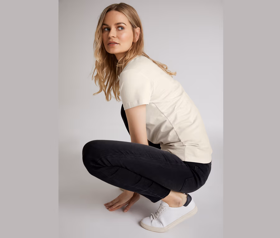Frau in der Hocke trägt Skinny-Jeans, T-Shirt und Turnschuhe.