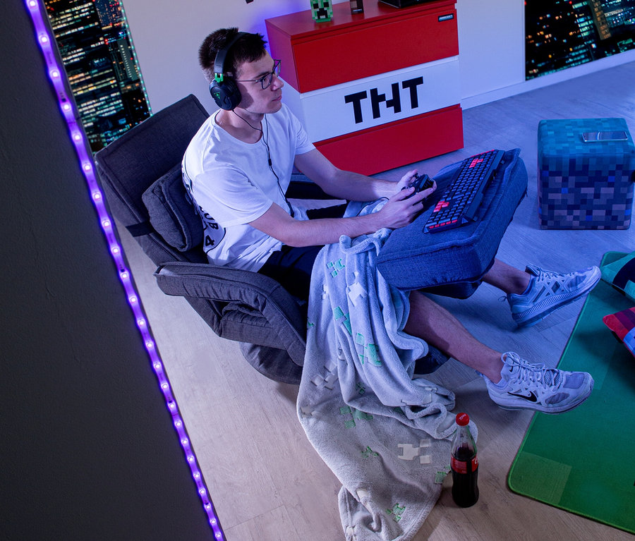 Ein junger Mann sitzt in einem roba Minecraft Loungesessel mit Beinen und Armlehne und spielt ein Videospiel.