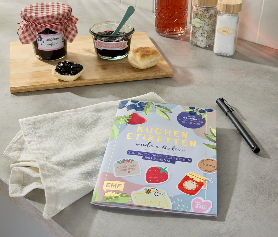 Marmeladengläser und ein Buch »Küchenetiketten« auf einer Küchentheke.