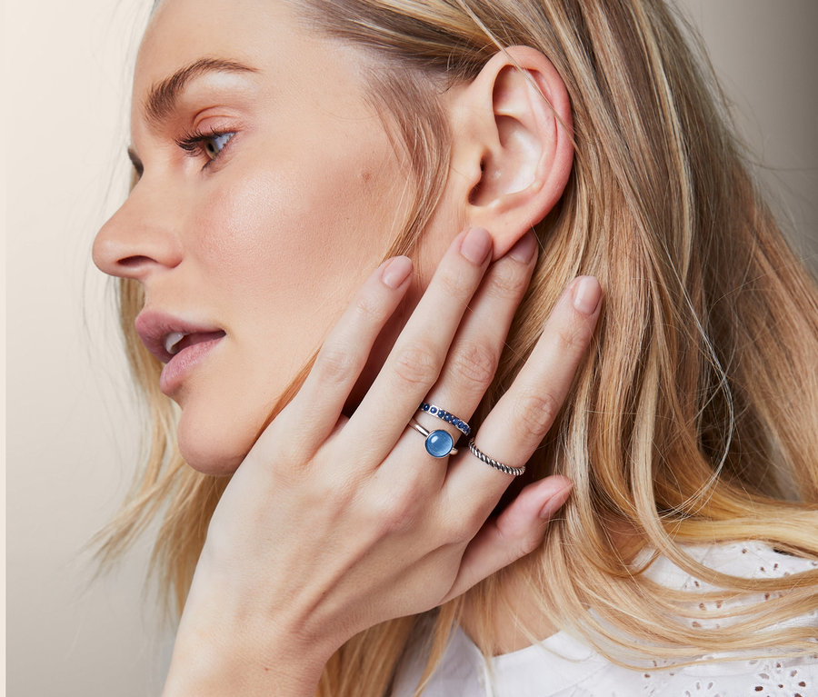 Blonde Frau trägt eine Uhr mit blauem Armband und ein 3er-Ring-Set am Finger.