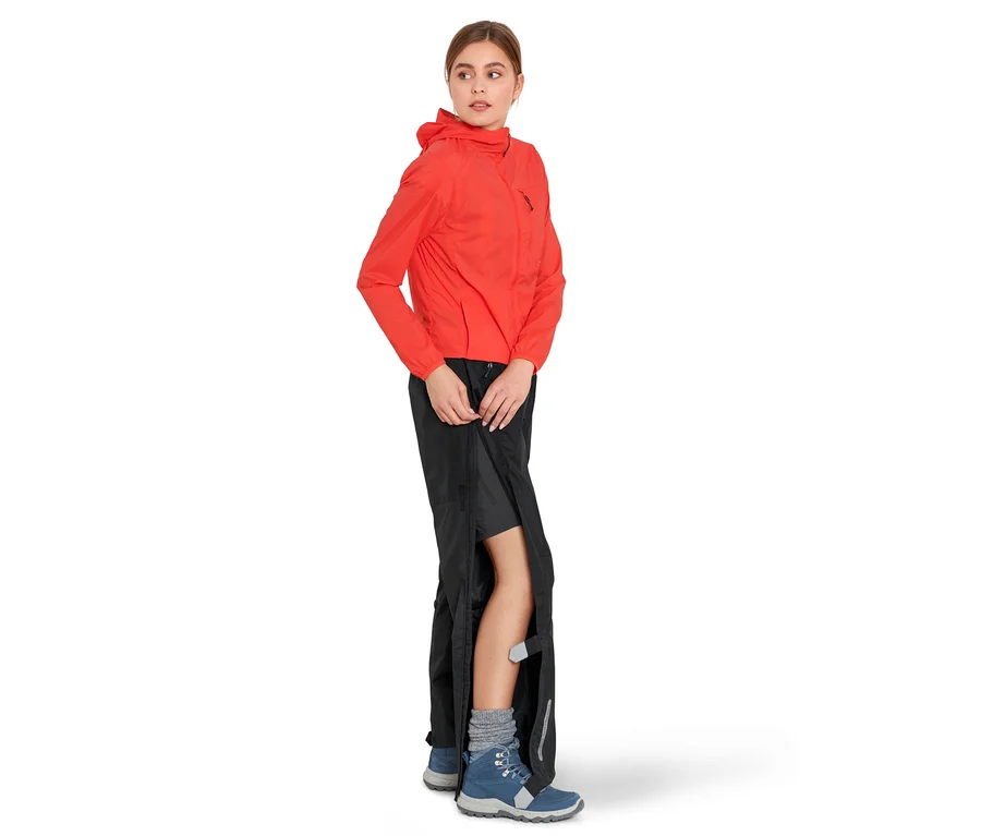 Frau schliesst eine schwarze High-Tech-Regenhose. Sie trägt eine orangefarbene Jacke und blaue Stiefel.