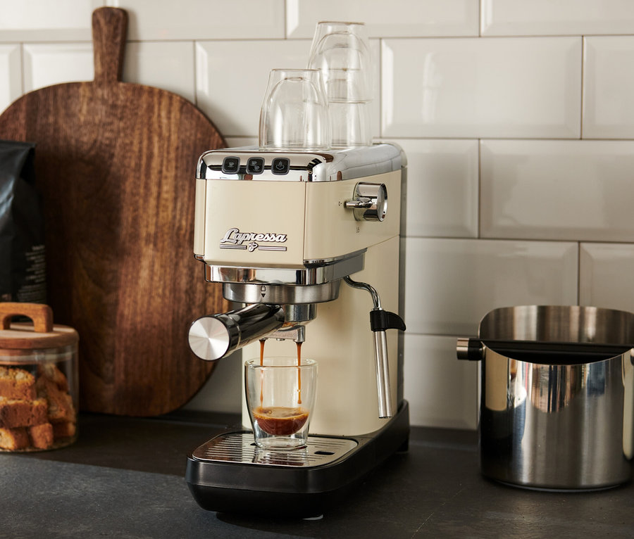 Eine creme »Lapressa« Siebträgermaschine bereitet Espresso in einem Glas zu.
