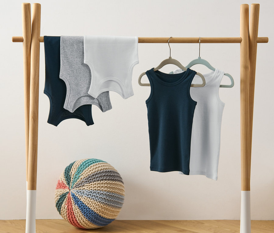 Fünf Jungen-Unterhemden hängen auf einem Kleiderständer.