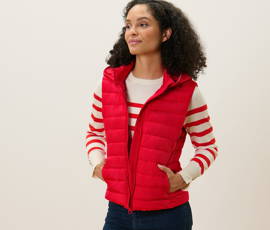 Frau trägt eine rote Steppweste mit Kapuze, steht und blickt nach links.