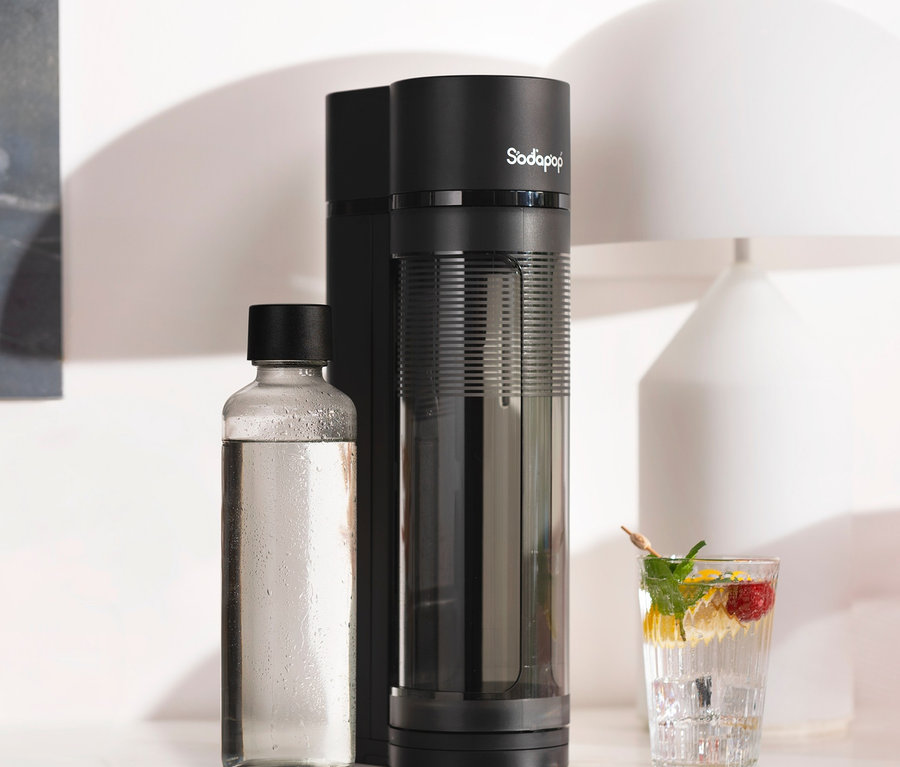 Schwarzer Sodapop Wassersprudler »Logan« steht neben einer Glasflasche und einem Glas mit Getränk.