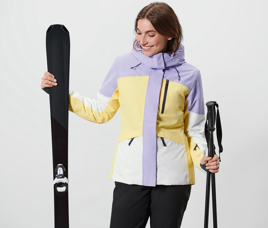 Frau hält Ski und Skistöcke. Sie trägt eine Skijacke.