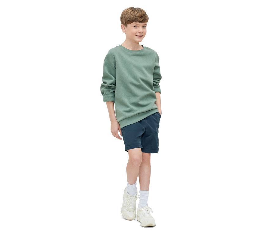 Junge posiert in grünem Sweatshirt und marineblauen Shorts. Kinder-Funktionshose.