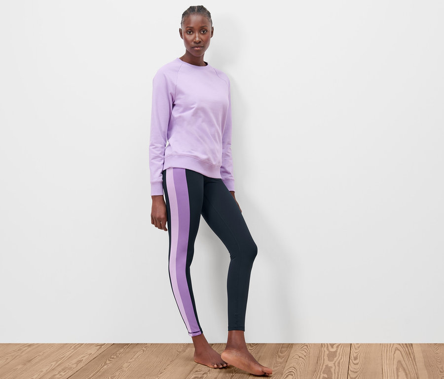 Frau steht, trägt lila Sweatshirt und dunkelblaue Sporttight.