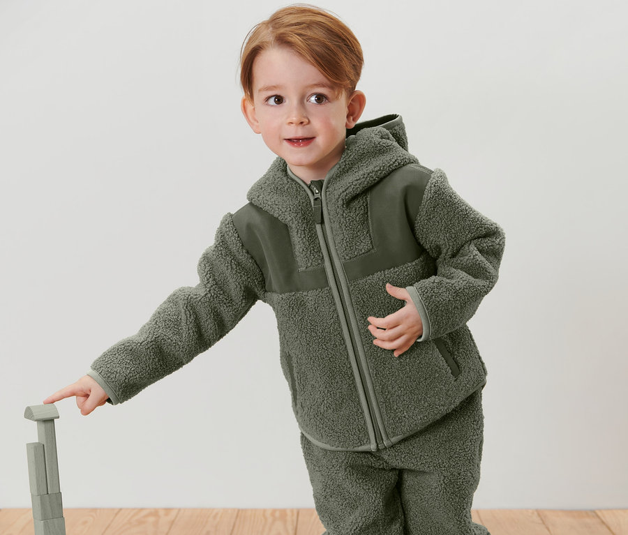 Junge trägt eine Kinder-Teddy-Jacke und spielt mit Holzspielzeug.