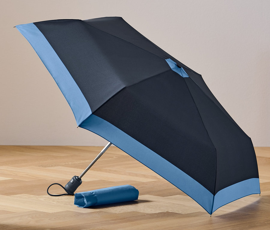 Ein schwarz-blauer Automatik-Taschenschirm liegt geöffnet auf einem Holzboden neben seiner Hülle.