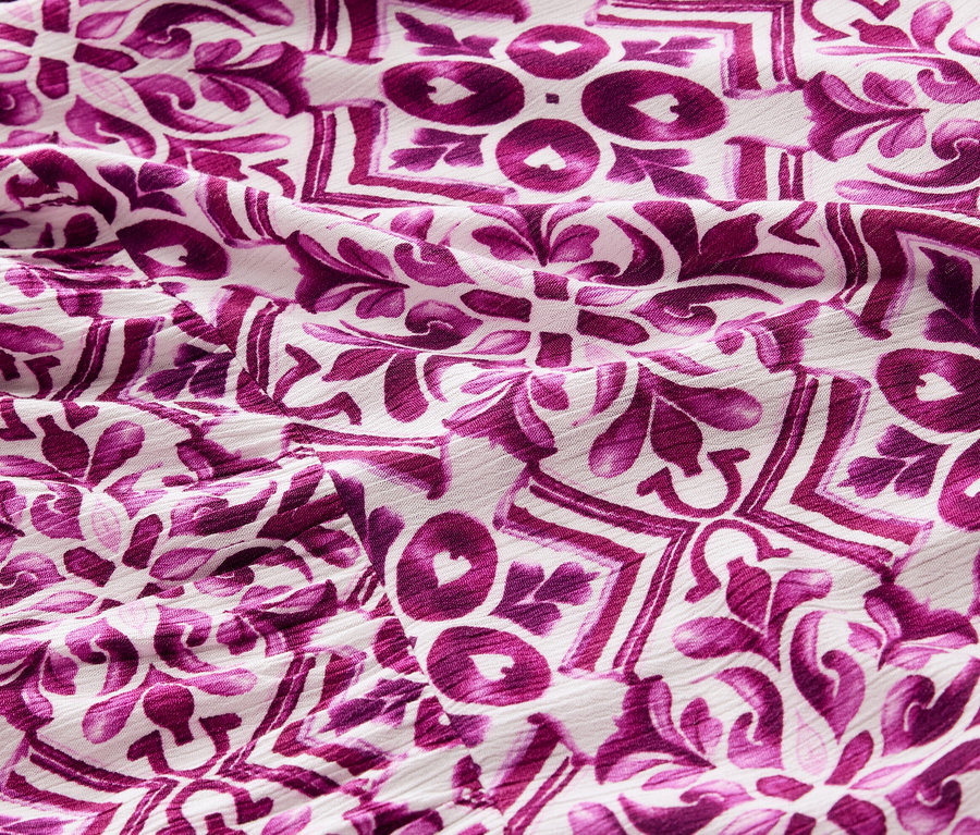 Detailansicht eines bedruckten Webkleides mit lila Muster.