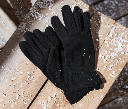 Schwarze Microfleece-Handschuhe liegen auf einer mit Schnee bedeckten Holzfläche.