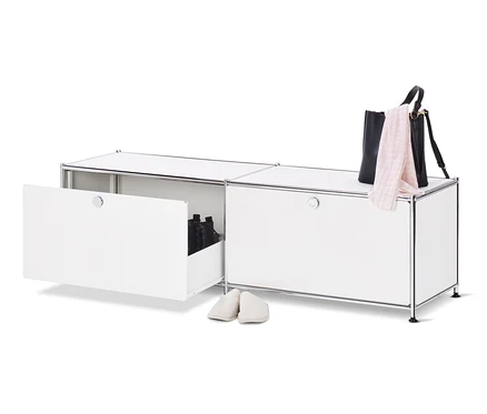 Ein geöffnetes, weißes Lowboard Metall »CN3« mit Schubladen und Schuhen darin, daneben ein Paar cremefarbene Hausschuhe, oben auf dem Schrank eine schwarze Handtasche und ein rosa Schal.