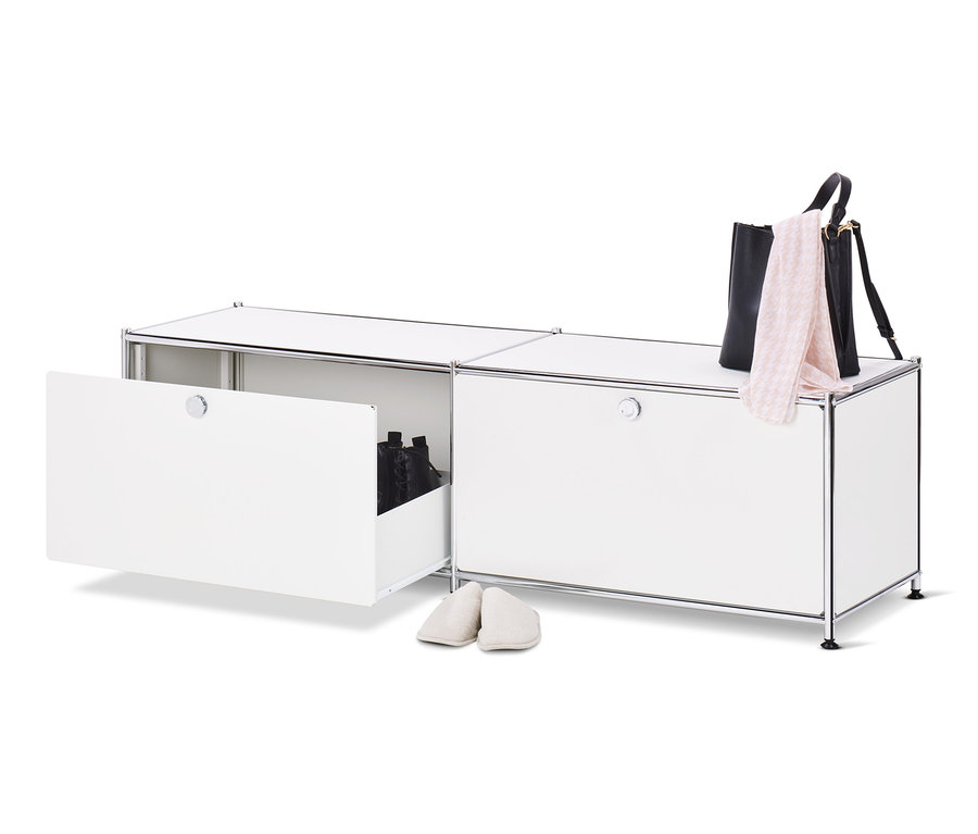 Ein geöffnetes, weißes Lowboard Metall »CN3« mit Schubladen und Schuhen darin, daneben ein Paar cremefarbene Hausschuhe, oben auf dem Schrank eine schwarze Handtasche und ein rosa Schal.