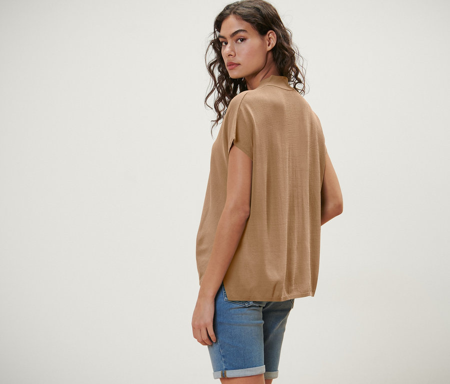 Frau blickt über die Schulter, trägt einen kurzärmligen Cardigan, beige.