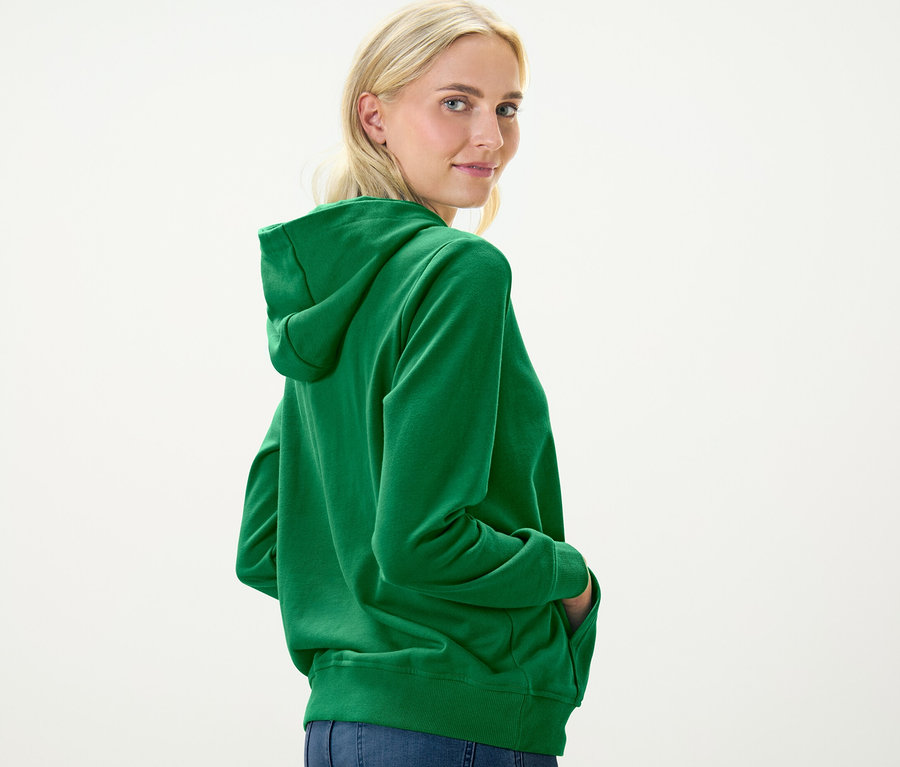 Blonde Frau blickt über die Schulter und trägt einen grünen Hoodie.