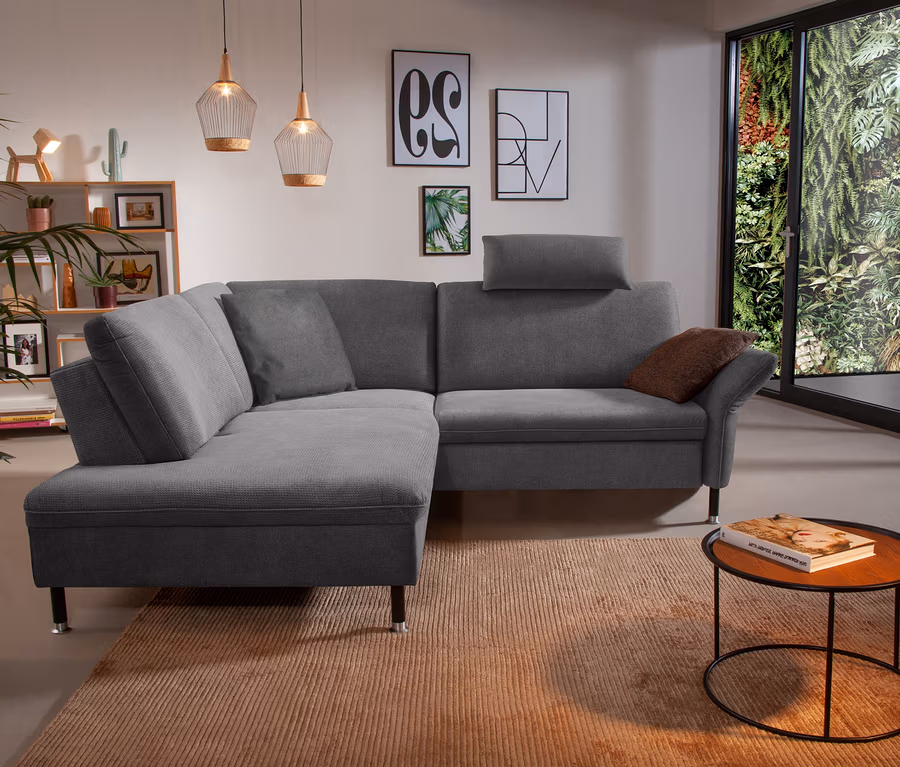 Wohnzimmer mit linksseitigem Ecksofa "Jonas" in Quarzgrau auf einem Teppich.