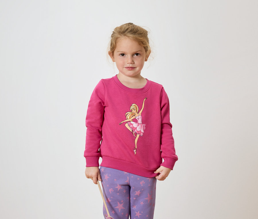 Mädchen in pinkem Pullover mit Ballerina-Motiv und lila Hose mit Sternenmuster.