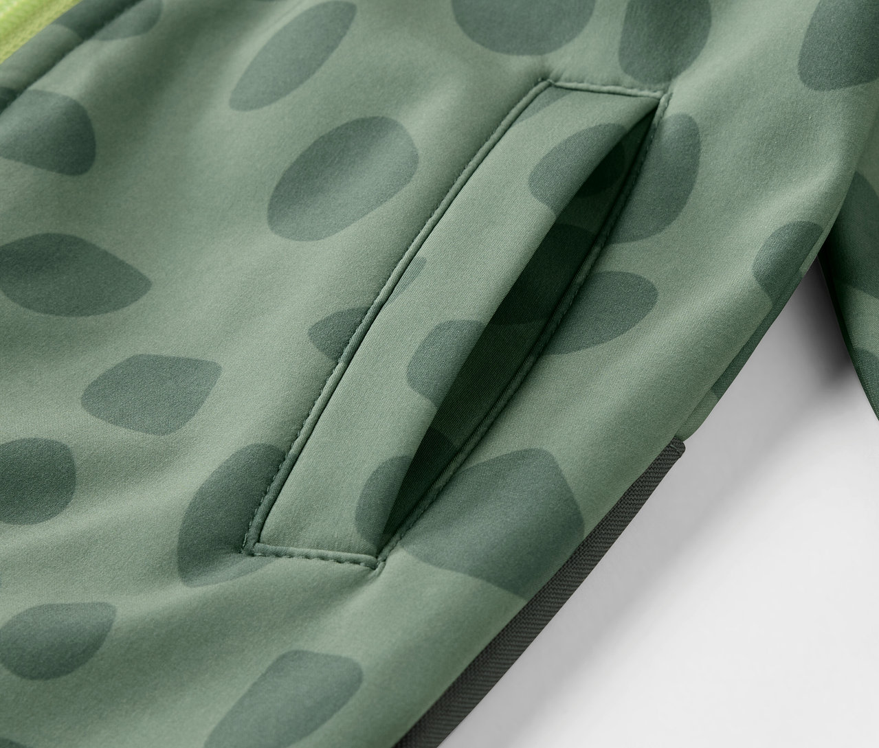 Detailansicht eines Kinder-Softshell-Einteilers mit Muster und Tasche.