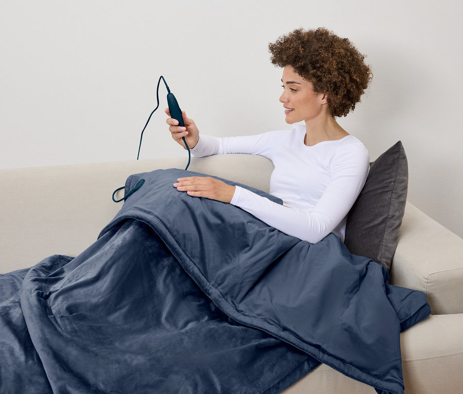 Frau sitzt auf der Couch und hält die Fernbedienung einer Heizdecke.