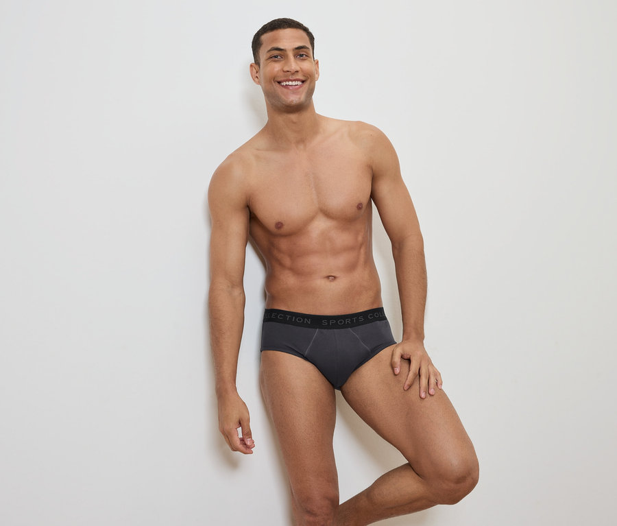 Lächelnder Mann mit freiem Oberkörper posiert in grauer Slip-Unterwäsche mit schwarzem Bund.