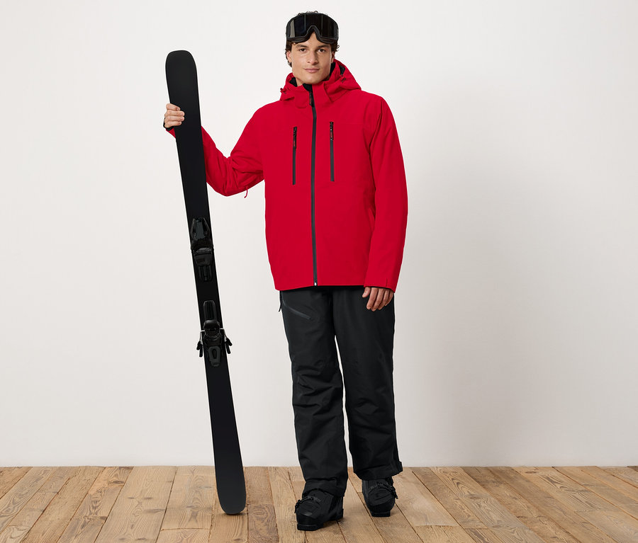 Mann in roter Jacke hält Ski.