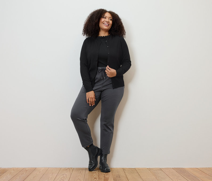 Frau posiert in Feinstrick-Cardigan, Joggpants mit Hahnentritt-Jacquard und schwarzem Shirt mit Wellenkante.