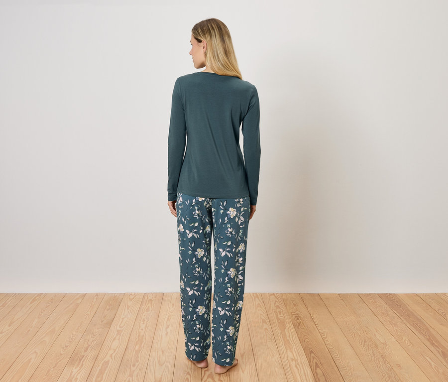 Frau steht mit dem Rücken zur Kamera und trägt einen grünen Schlafanzug mit langen Ärmeln und eine geblümte Hose.