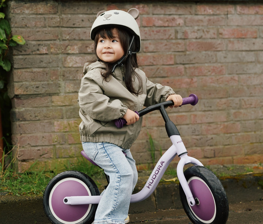 Mädchen auf Laufrad trägt HUDORA Kinderhelm, Beary, 48–52 cm.