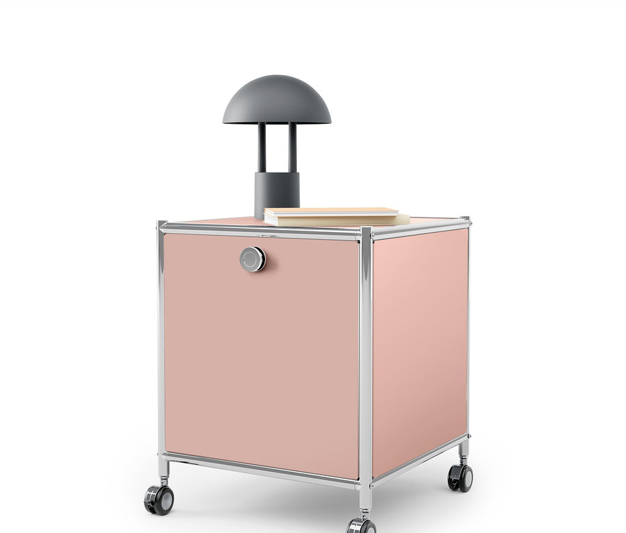 Rosa Rollcontainer mit Chromrahmen und grauer Lampe darauf.