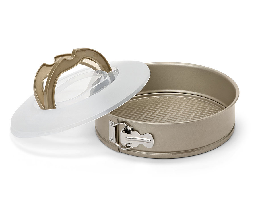 Eine goldene Springform mit abnehmbarem Boden und transparentem Deckel liegt auf einem weißen Hintergrund.