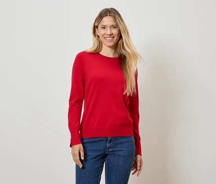 Frau mit blonden Haaren posiert in einem roten Pullover und blauen Jeans.