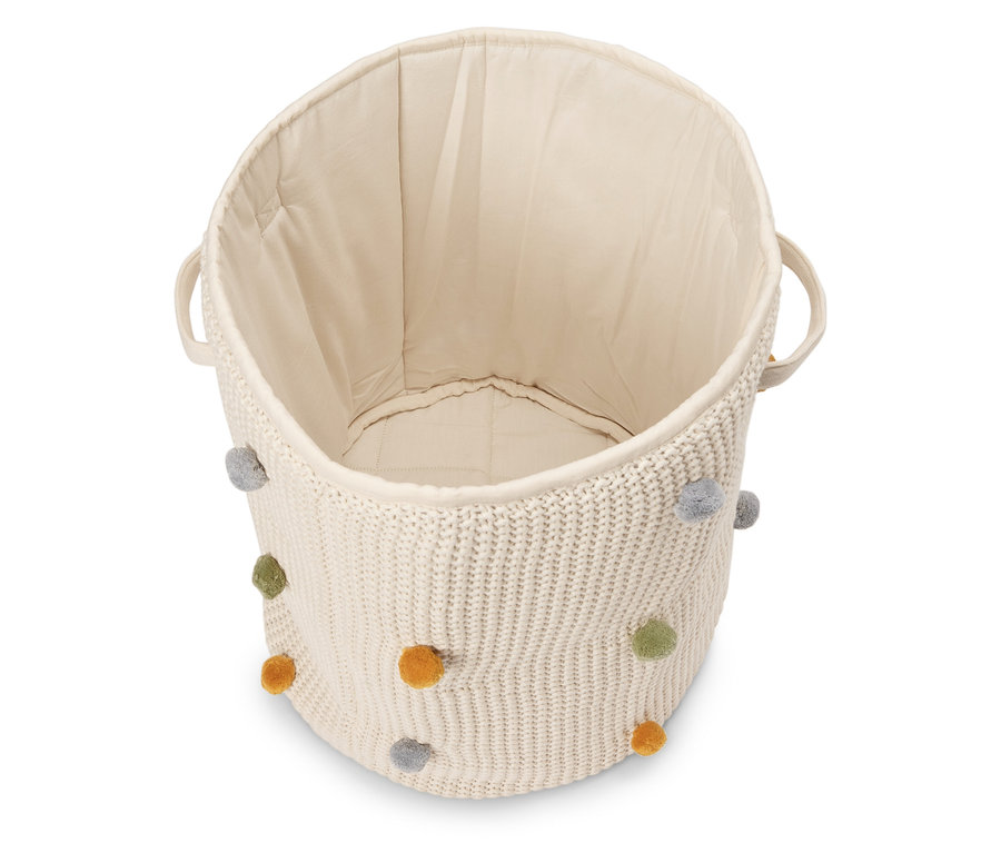Korb aus cremefarbenem Strick mit farbigen Bommeln, leer von oben fotografiert.