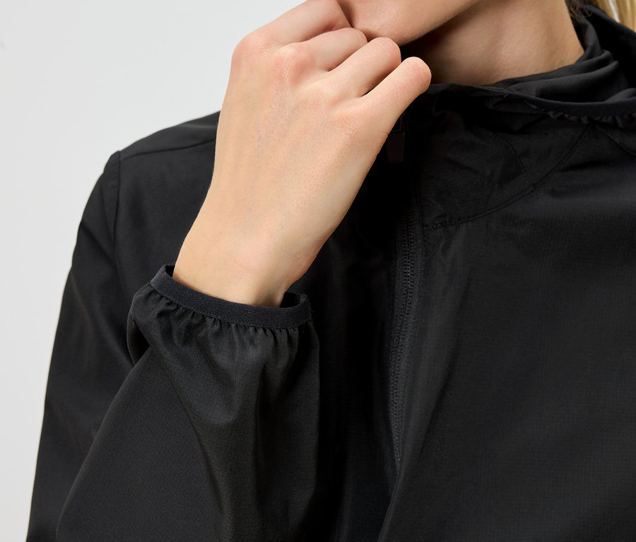 Nahaufnahme einer Person, die eine schwarze Regenjacke mit Kapuze trägt und mit der Hand den Reißverschluss schließt.