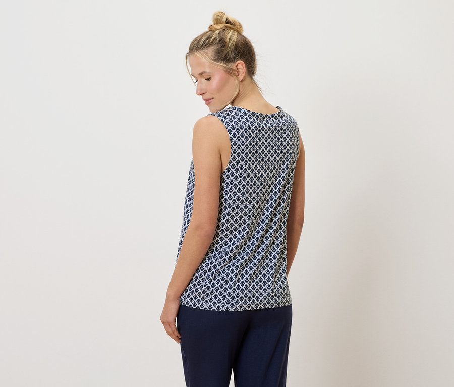 Blonde Frau mit Dutt trägt ein blau-weiß gemustertes Tanktop und eine marineblaue Hose, von hinten gesehen.