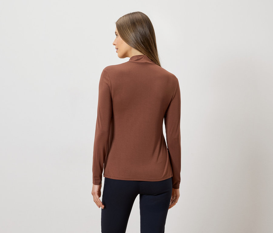 Frau von hinten, trägt ein braunes Langarmshirt und eine dunkle Hose vor einem weißen Hintergrund.