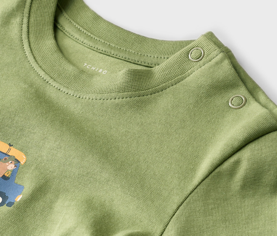 Nahaufnahme eines hellgrünen T-Shirts mit Rundhalsausschnitt und Druck, sowie zwei Knöpfen an der Schulter.