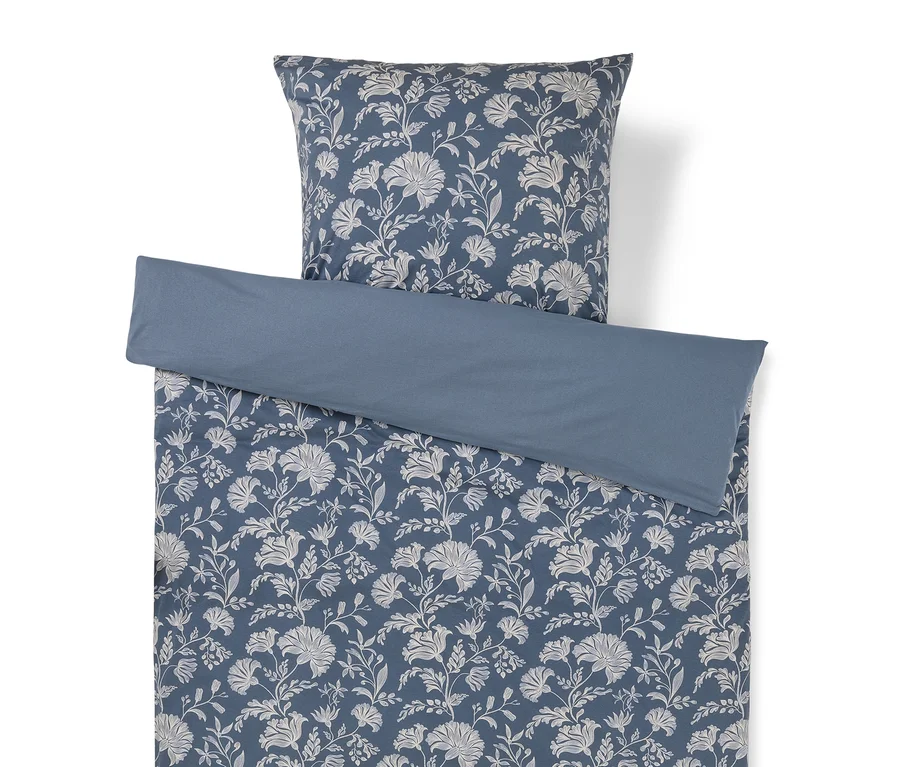 Ein blaues Bettwäscheset mit weißem Blumenmuster und passendem Kissenbezug, mit einem einfarbigen blauen Umschlag oben.