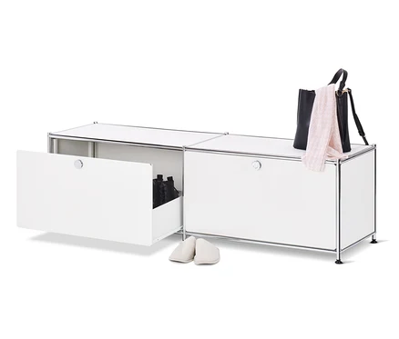 Ein geöffnetes, weißes Lowboard Metall »CN3« mit Schubladen und Schuhen darin, daneben ein Paar cremefarbene Hausschuhe, oben auf dem Schrank eine schwarze Handtasche und ein rosa Schal.