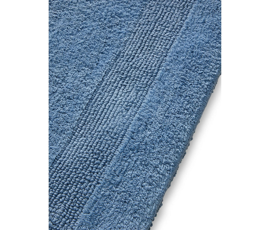 Nahaufnahme einer blauen Badematte mit Streifenmuster. Die Matte hat eine flauschige Textur mit einem mittigen diagonalen Streifen aus festeren Schlingen.
