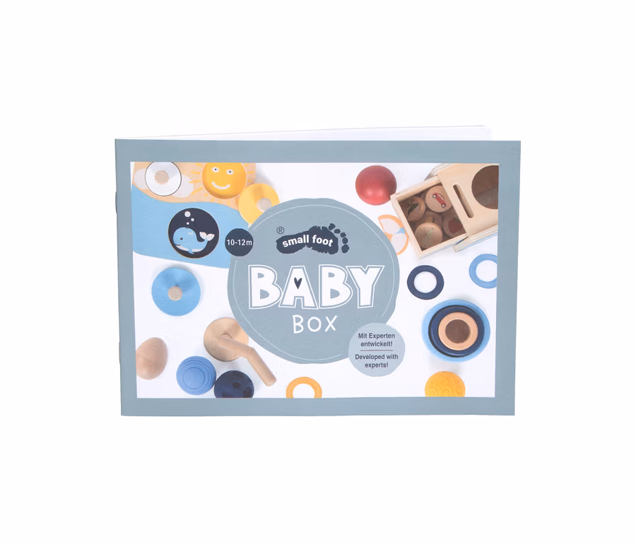 Verpackung der small foot Baby-Box für 10-12 Monate, mit einem grauen Etikett und Abbildungen von bunten Holzspielzeugen wie Ringen, Kugeln und Formen auf weißem Hintergrund.