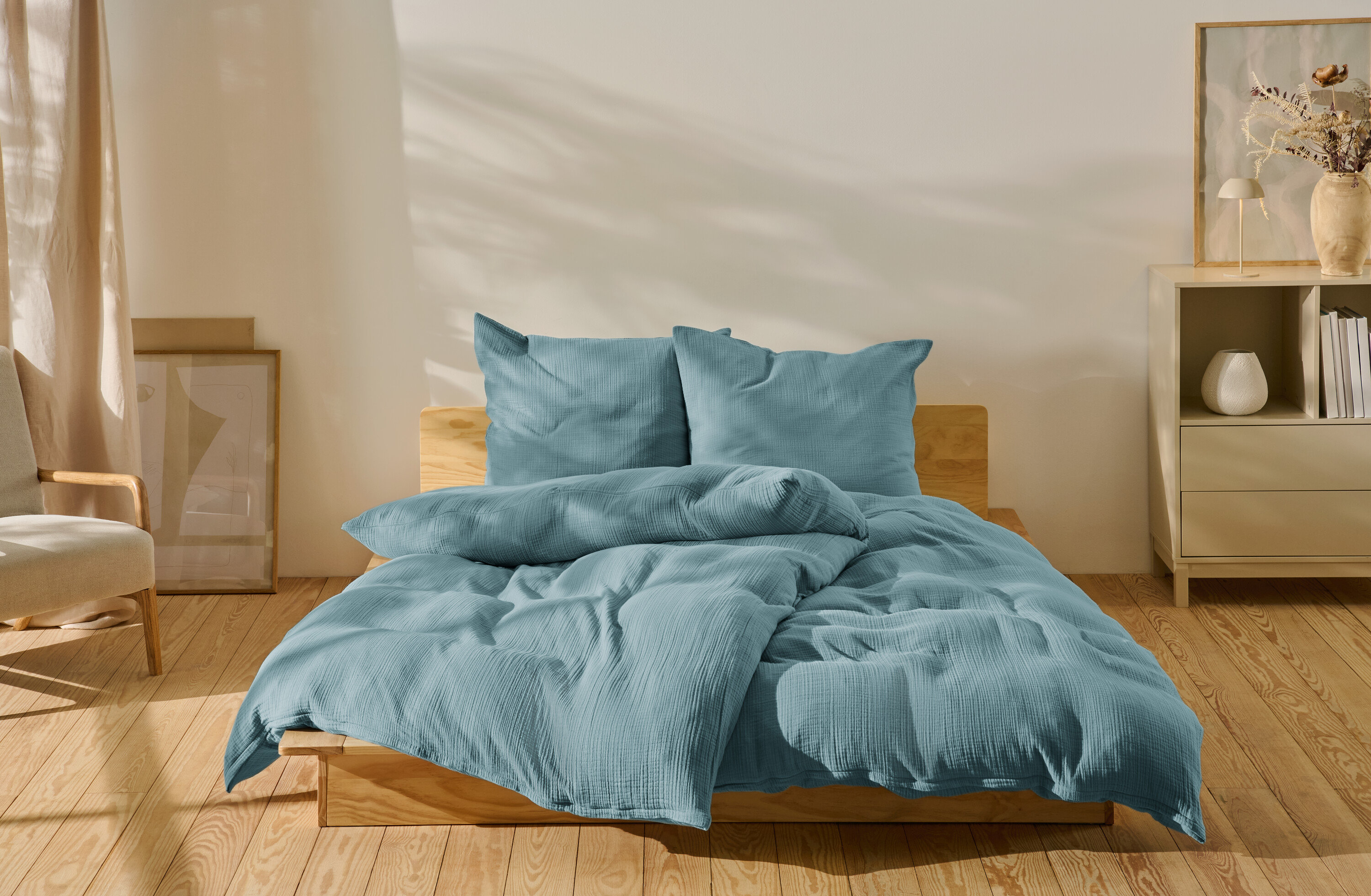 Blaue Musselin-Bettwäsche in Normalgröße und Übergröße auf einem Bett.