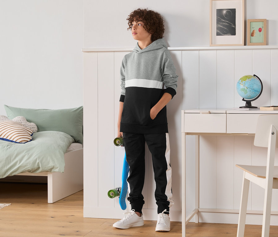 Junge steht im Zimmer und trägt eine 2-teilige Sweat-Kombi.