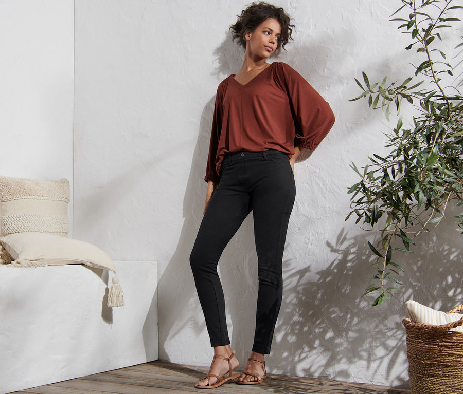 Frau posiert in schwarzen Jeggings, brauner Bluse und Sandalen.