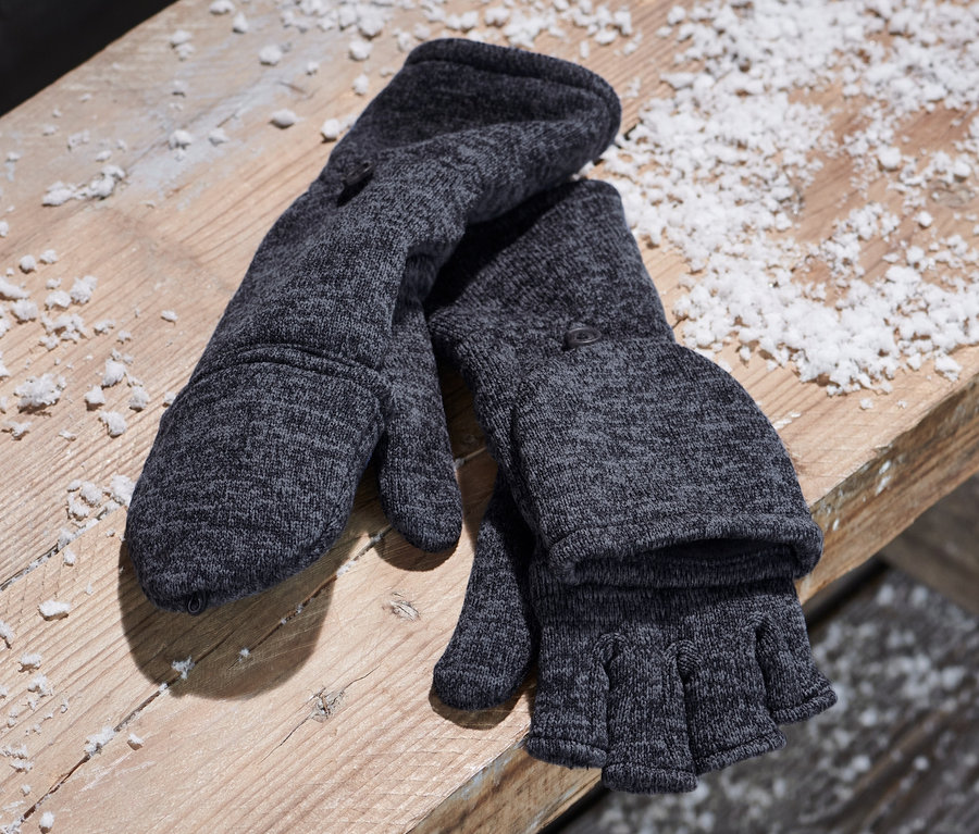 Blaue Strickfleece-Klappfäustlinge liegen neben einem Canvas-Rucksack auf einer Holzbank.