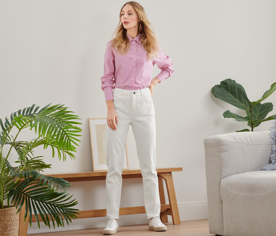 Frau posiert in rosa Hemd und weißen Straightfit-Jeans.