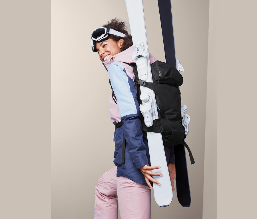 Frau lächelt und trägt Ski mit Ski-Rucksack.