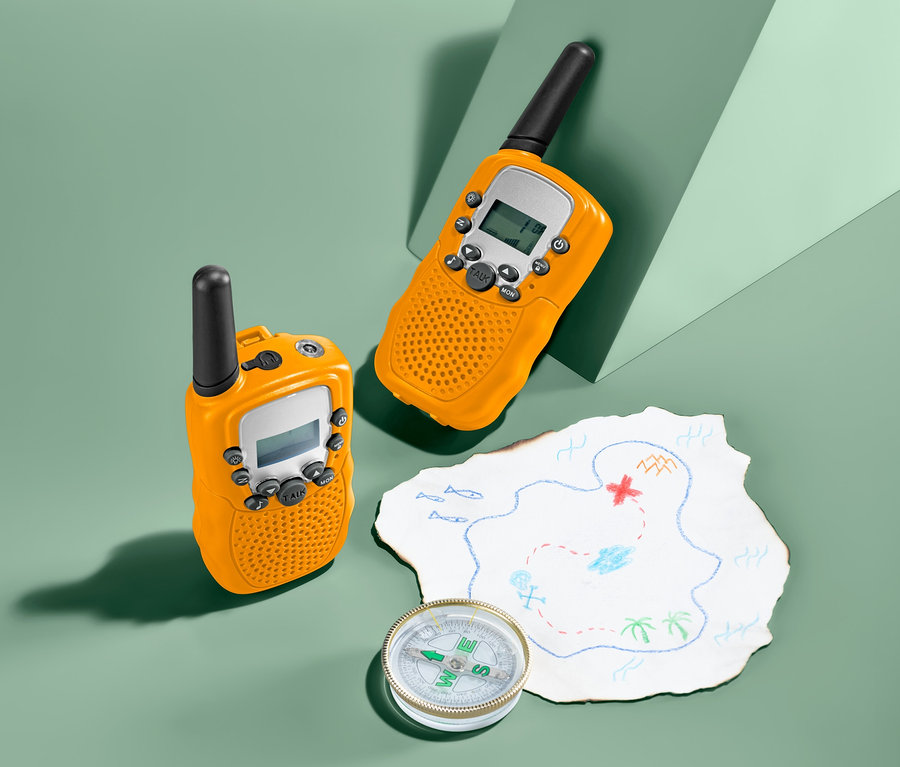 Zwei gelbe 2 Walkie-Talkies liegen neben einer Schatzkarte und einem Kompass auf grünem Grund.