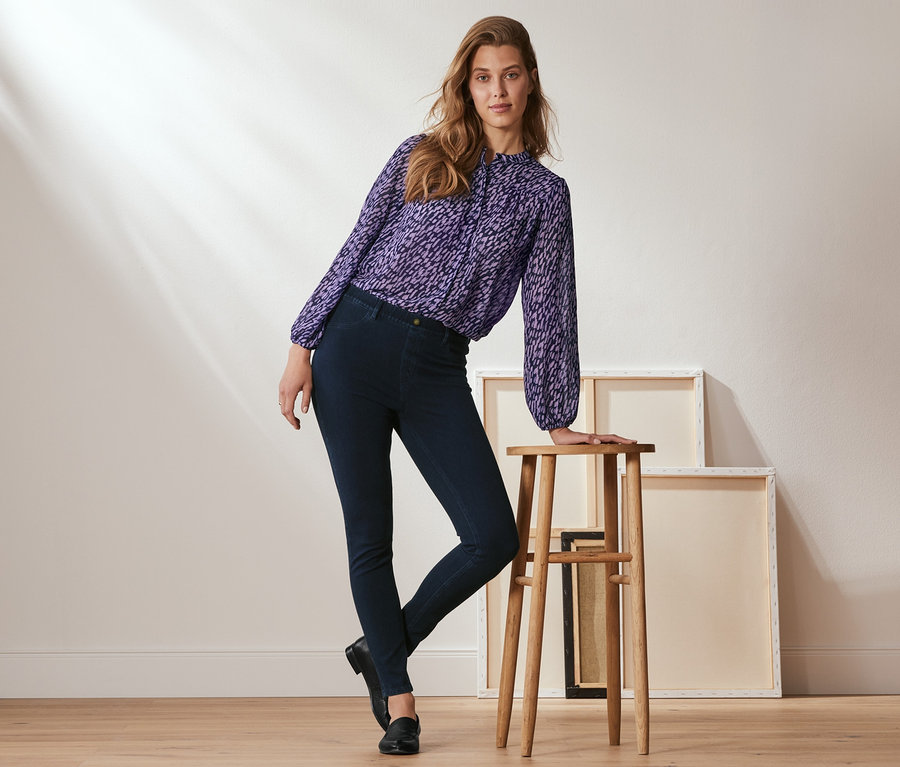 Frau posiert an einem Holzschemel, sie trägt dunkle Denim-Jeggings.