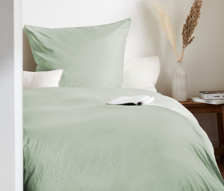 Hellgrüne Seersucker-Bettwäsche in Normal- und Übergröße auf einem Bett mit einem Buch.
